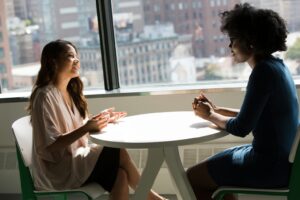 Two people talking across a table by a window